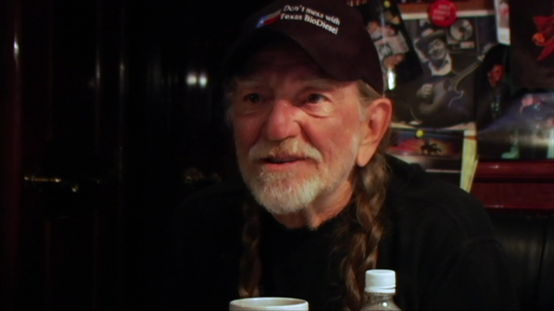Willie Nelson speaks during a formal interview session before transitioning to a musical segment featuring him playing an acoustic guitar.
