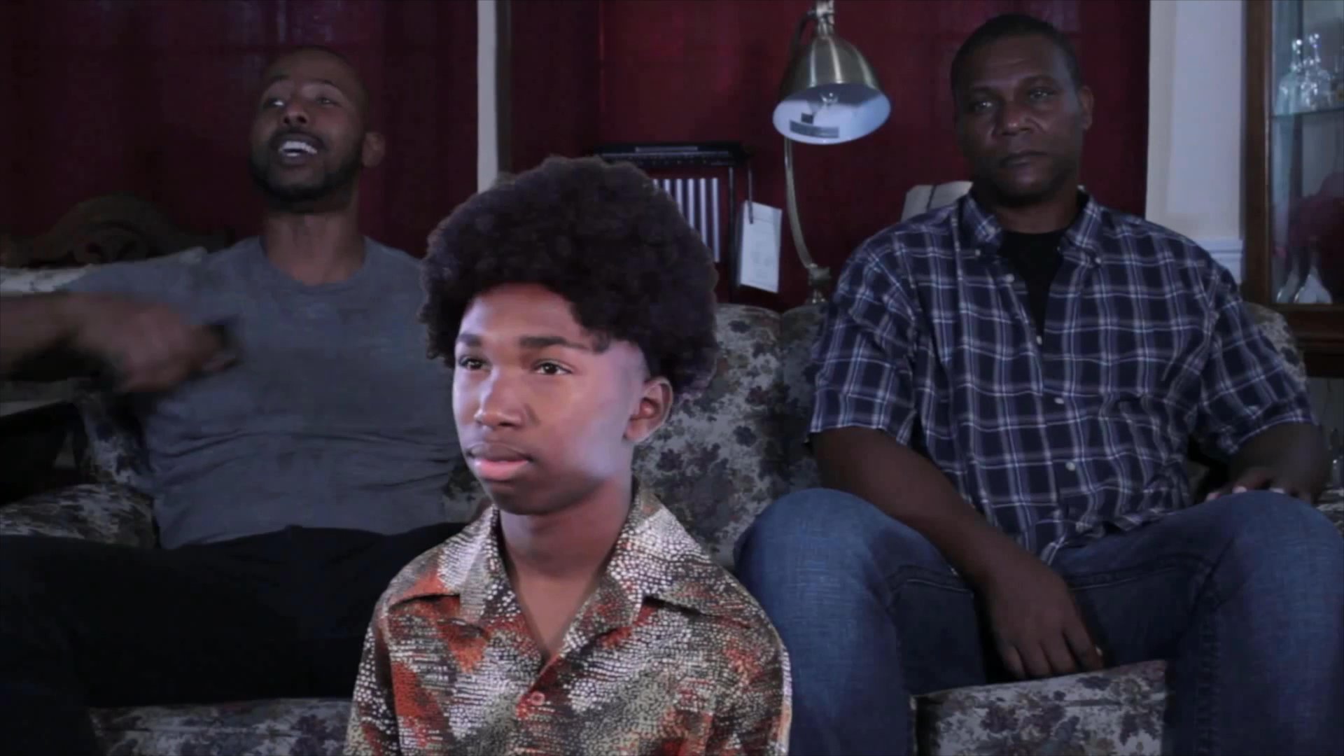 A young man and two older adults engage in a discussion while sitting on a couch in a residential living area.