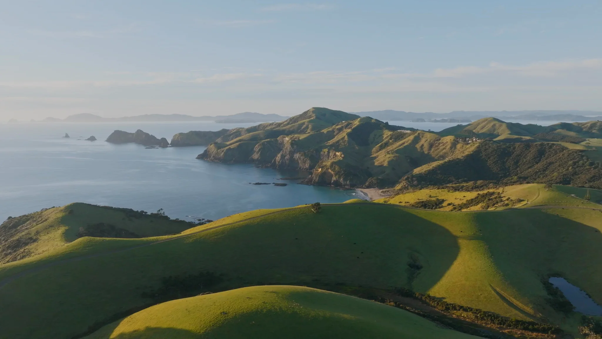 Rolling green pasture above the bay, with headlands and islands beyond
