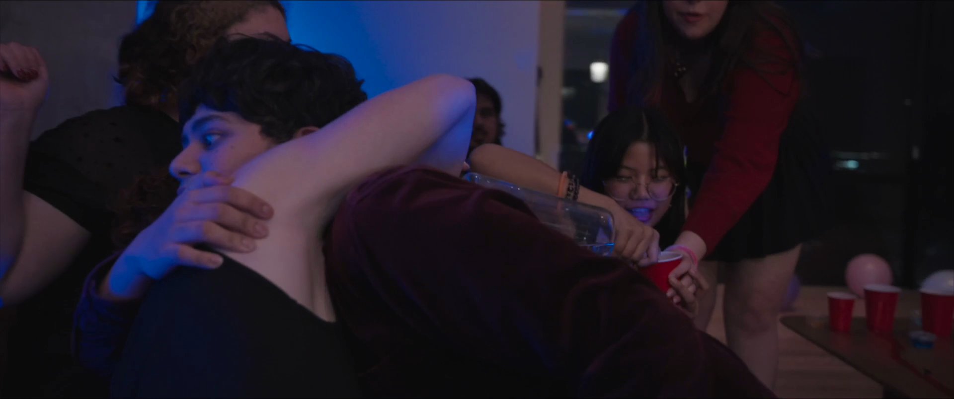 Young adults engage in spirited conversation and celebrate together at an evening social gathering. The atmosphere transitions from lighthearted interaction to shared indulgence as guests socialize in a home setting.