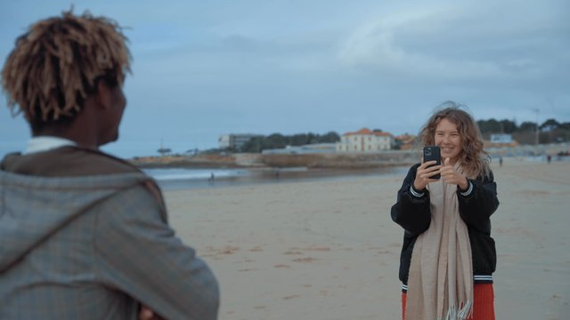 A girl photographs her male friend on the beach