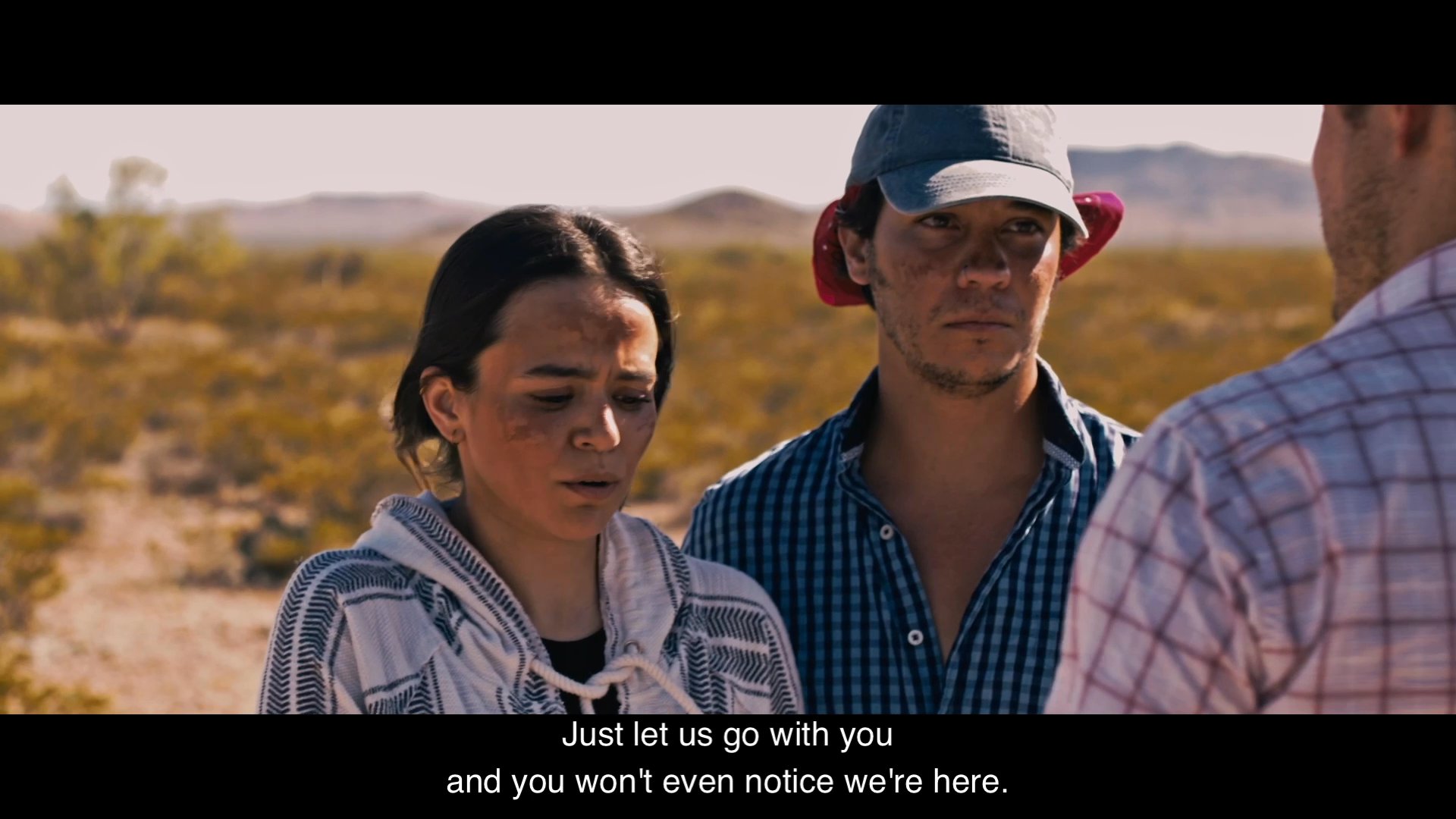 Two individuals attempt to negotiate passage with a man in a desert environment, facing firm rejection and hostility. Despite the resistance, they persist in their plea while navigating the high-stakes encounter.