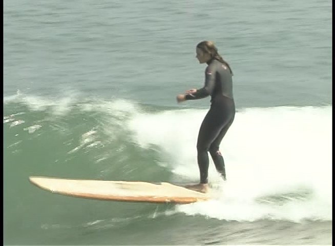 A surfer skillfully navigates a longboard across the surface of an ocean wave while wearing a wetsuit.