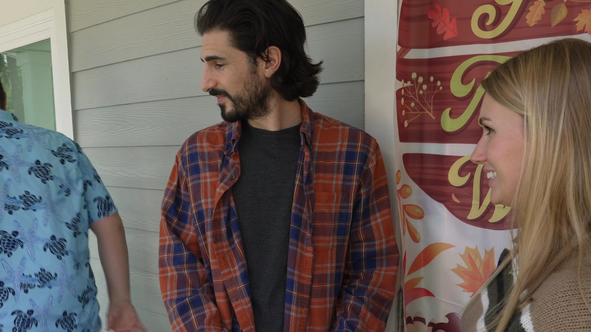 Two men and a woman engage in a friendly, professional interaction in front of a Thanksgiving-themed banner. The group shares a moment of appreciation and collaborative spirit in a seasonal setting.