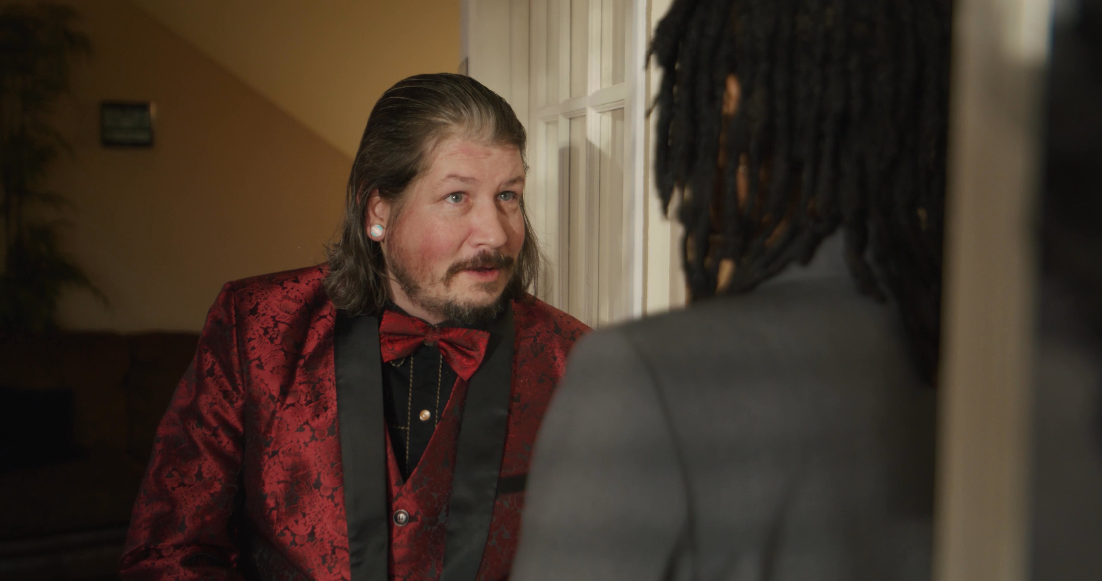 A professional in a business suit engages in a conversation with a visitor wearing a formal red blazer. The exchange takes place in a bright, formal lobby setting.