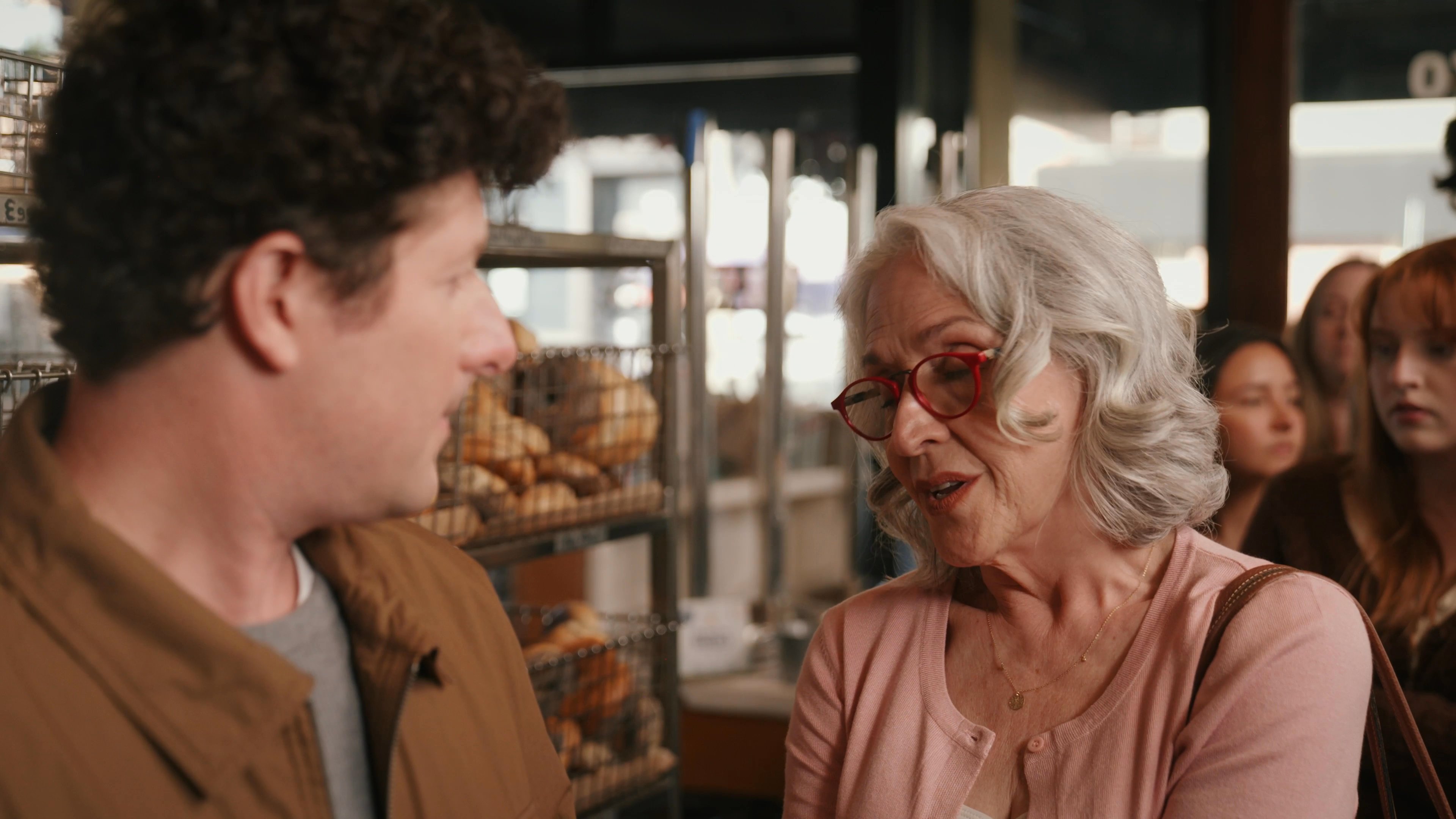 A man engages in a focused conversation with a woman inside a retail bakery. The pair discusses product details while standing in front of shelves stocked with baked goods.