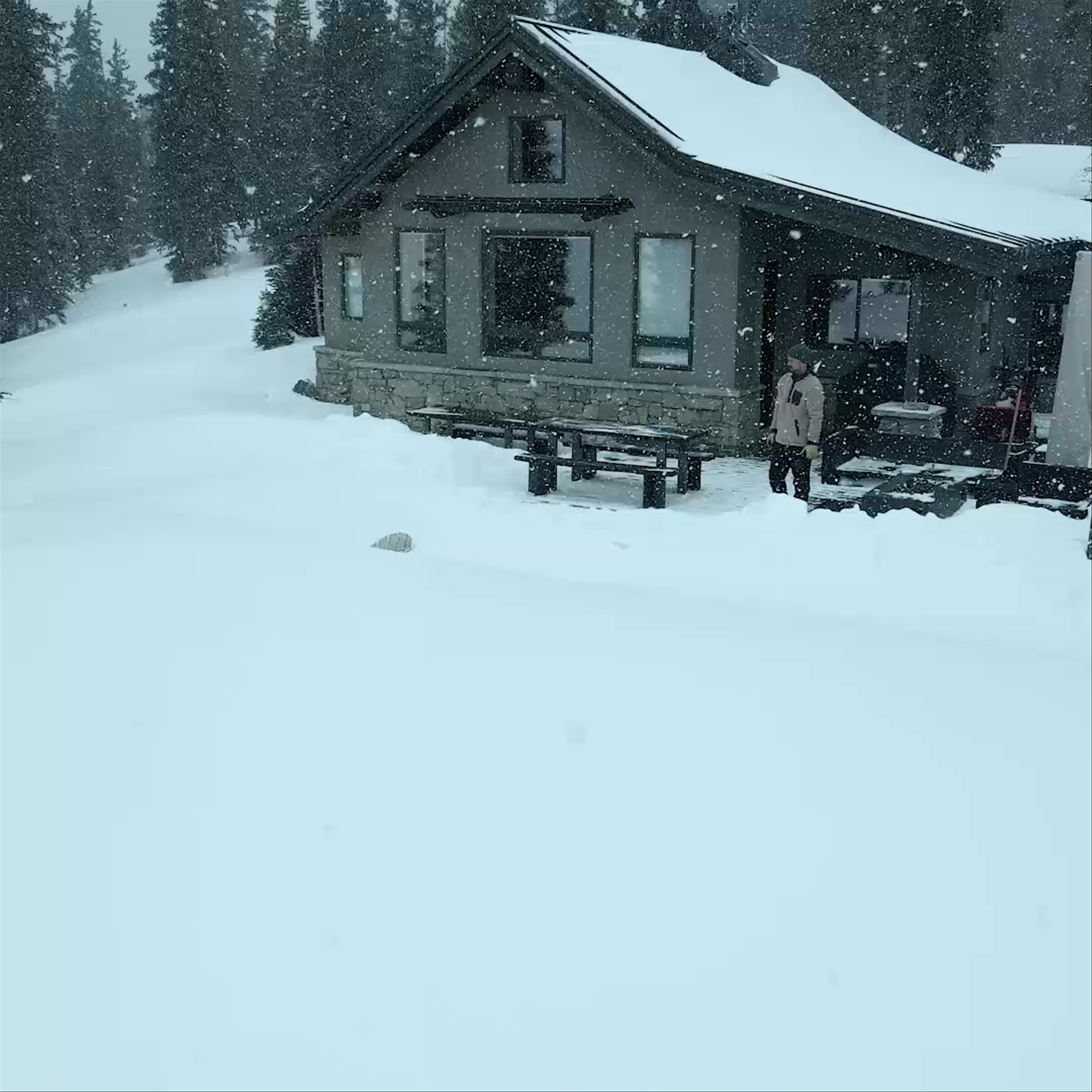 Video drone of man outside cabin pulling back to reveal full snowy mountain