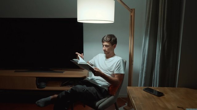 Un hombre está leyendo un libro por la noche.