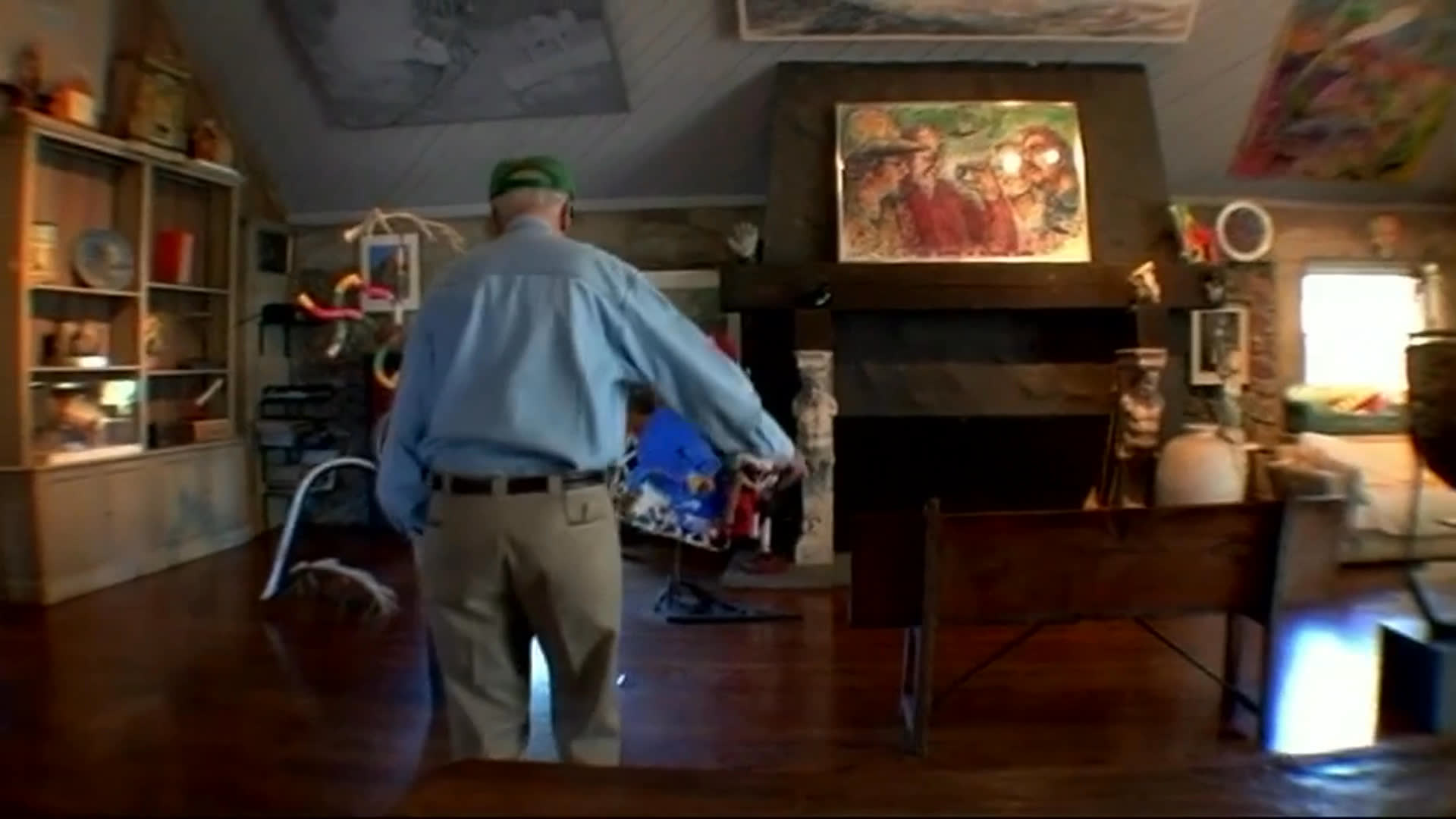 An older man walks through an art-filled living room as he recalls post-dinner dancing and entertaining guests. A black-and-white photograph of him with his wife accompanies his reflection on her departure.
