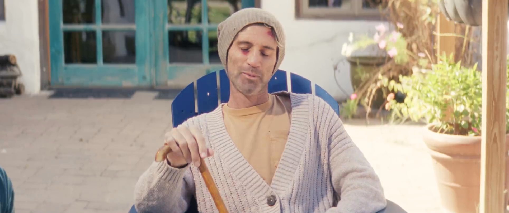 Two men engage in a relaxed, thoughtful conversation while situated on a patio overlooking a lush orchard. The scene highlights a connection between generations as they share a moment of quiet reflection.