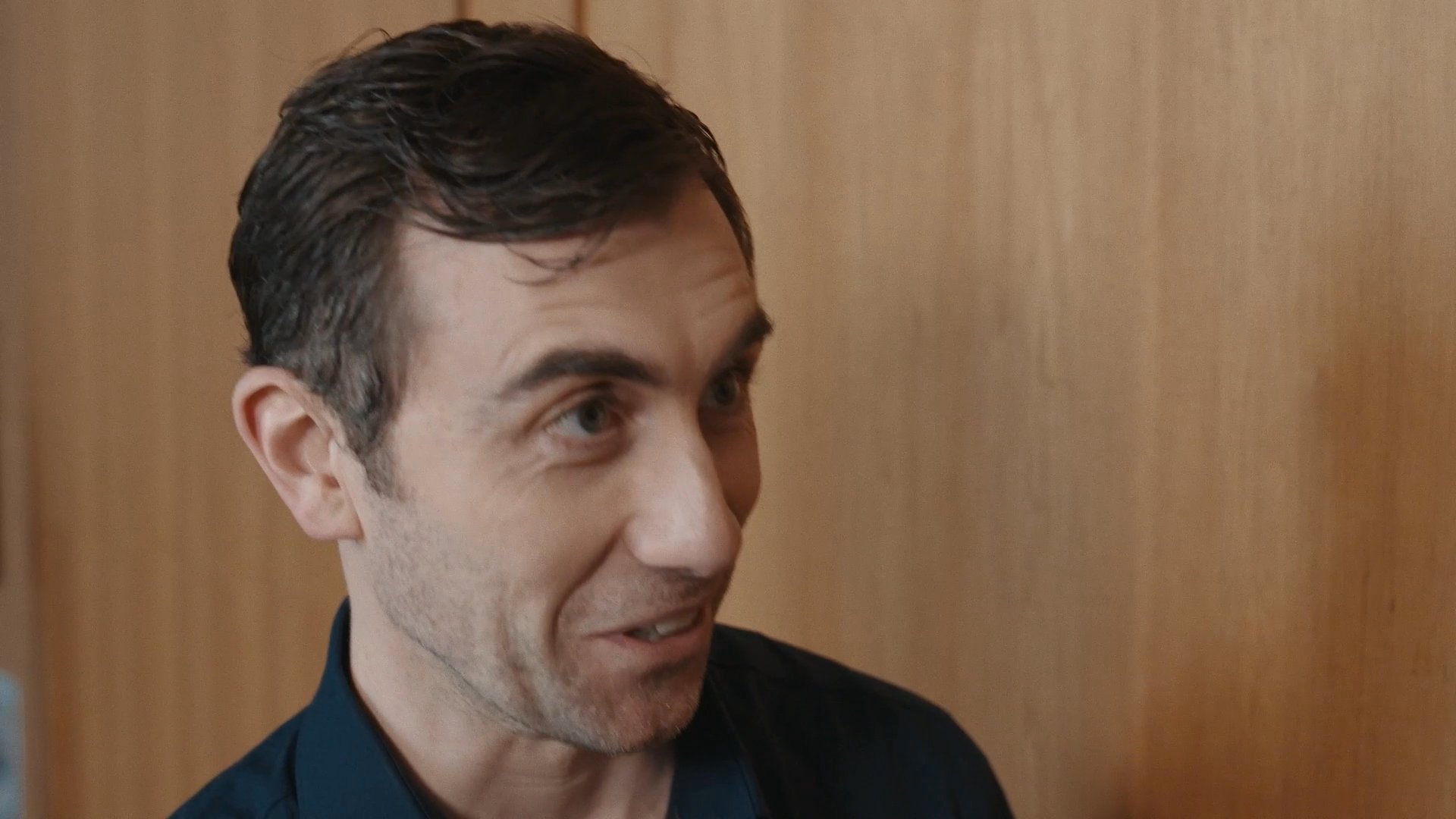 Two male professionals engage in an animated, friendly conversation within a conference room setting. Their interaction is marked by mutual engagement and positive rapport.