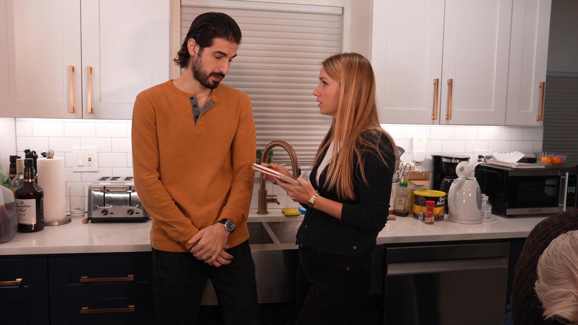 A group of individuals coordinates tasks in a kitchen, with members actively writing notes and discussing plans for food preparation.