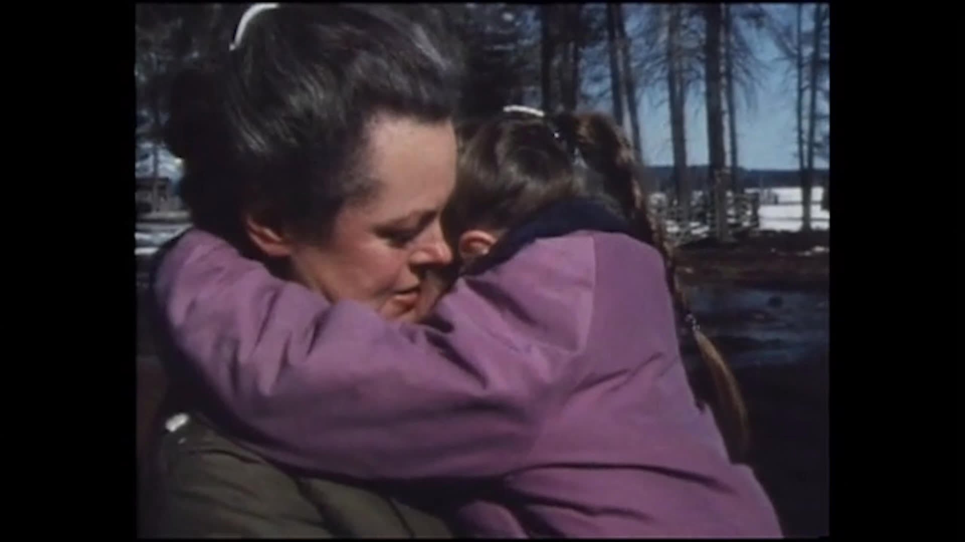 After a brief cry beside a large animal, a woman embraces a child in a purple jacket in a snowy, wooded yard. They talk and laugh as she asks whether the child’s big toe or little toe was hurt.