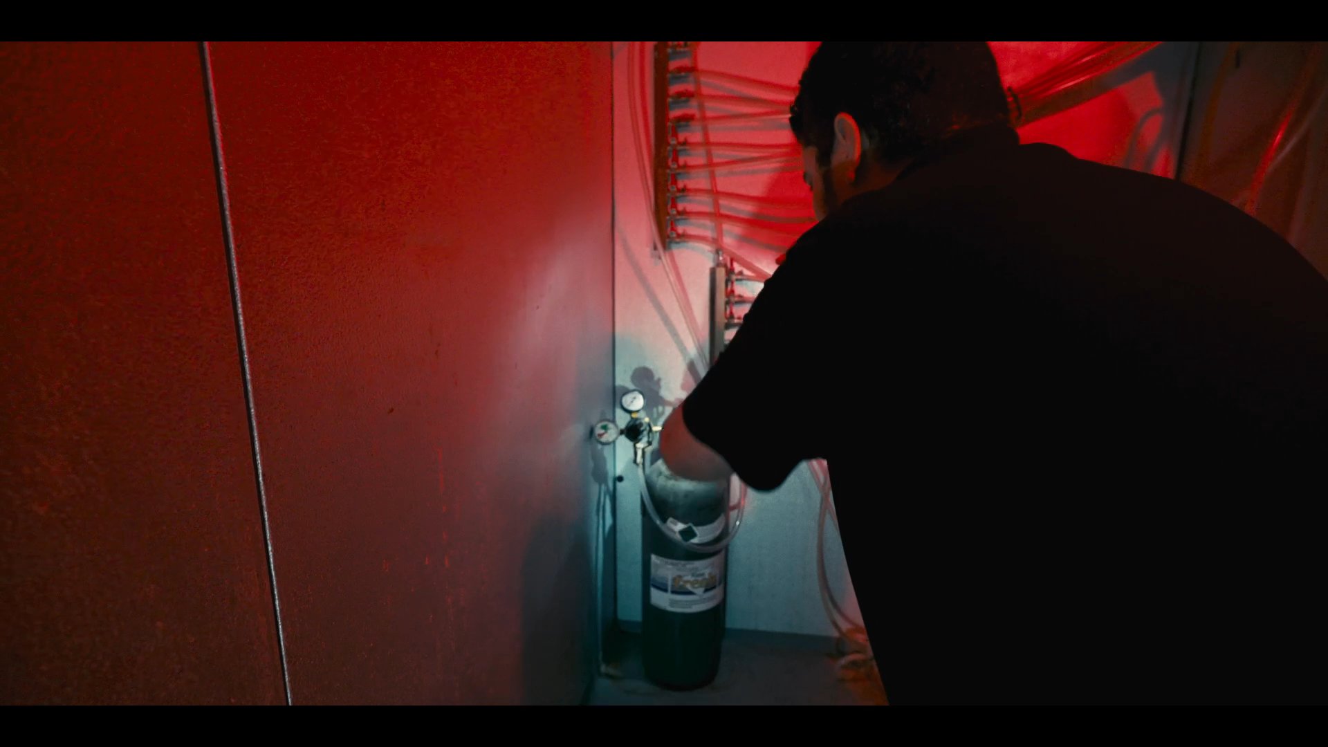 A technician performs technical adjustments on equipment within an industrial facility during the night, contrasted against an aerial view of a city skyline.
