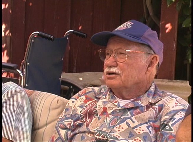 An elderly man named Bill Grace recounts historical events, contrasted with night vision surveillance footage of a dark stadium.