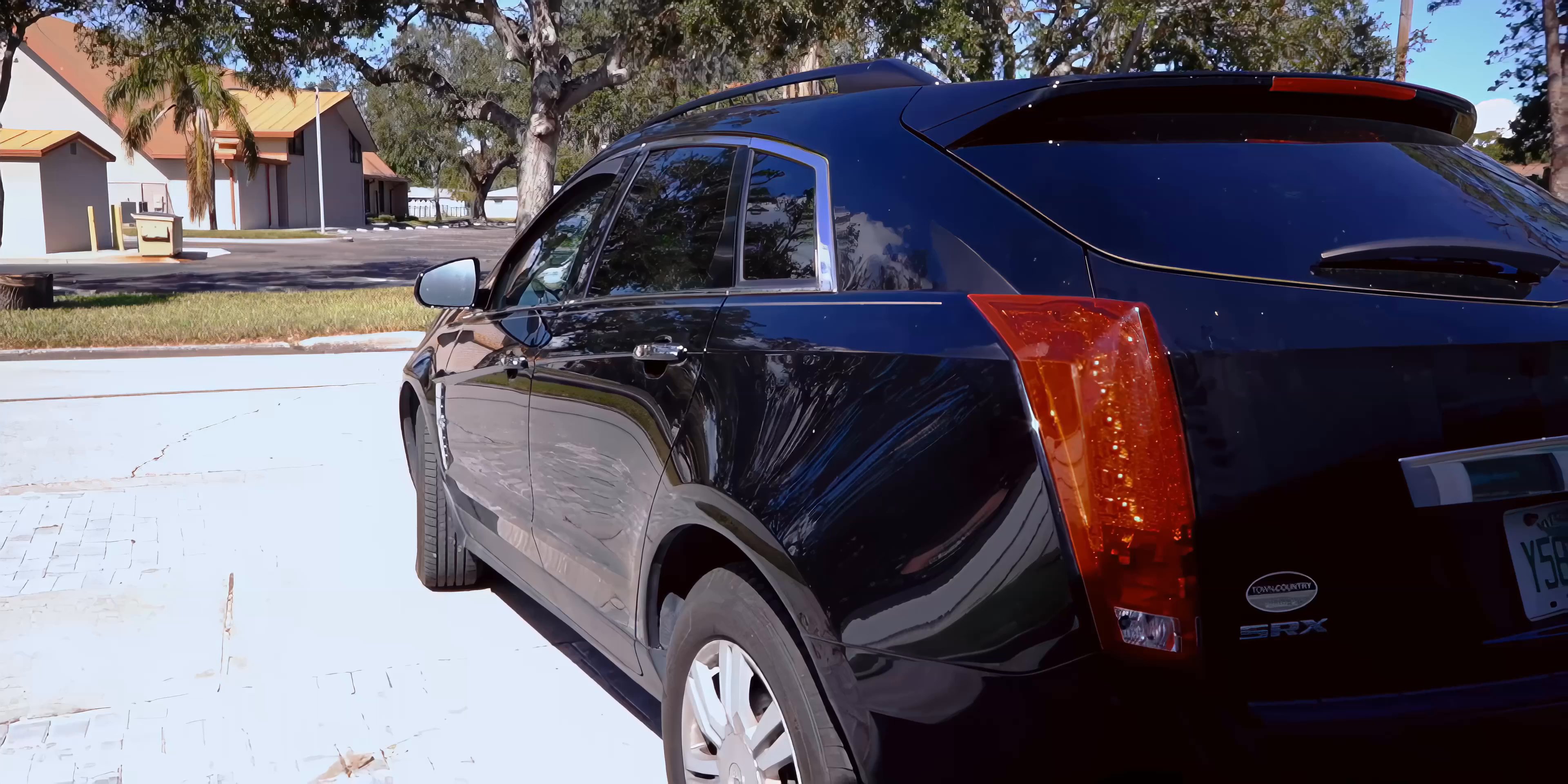 A man enters a black Cadillac SRX parked in a sunny lot and drives away from the camera.
