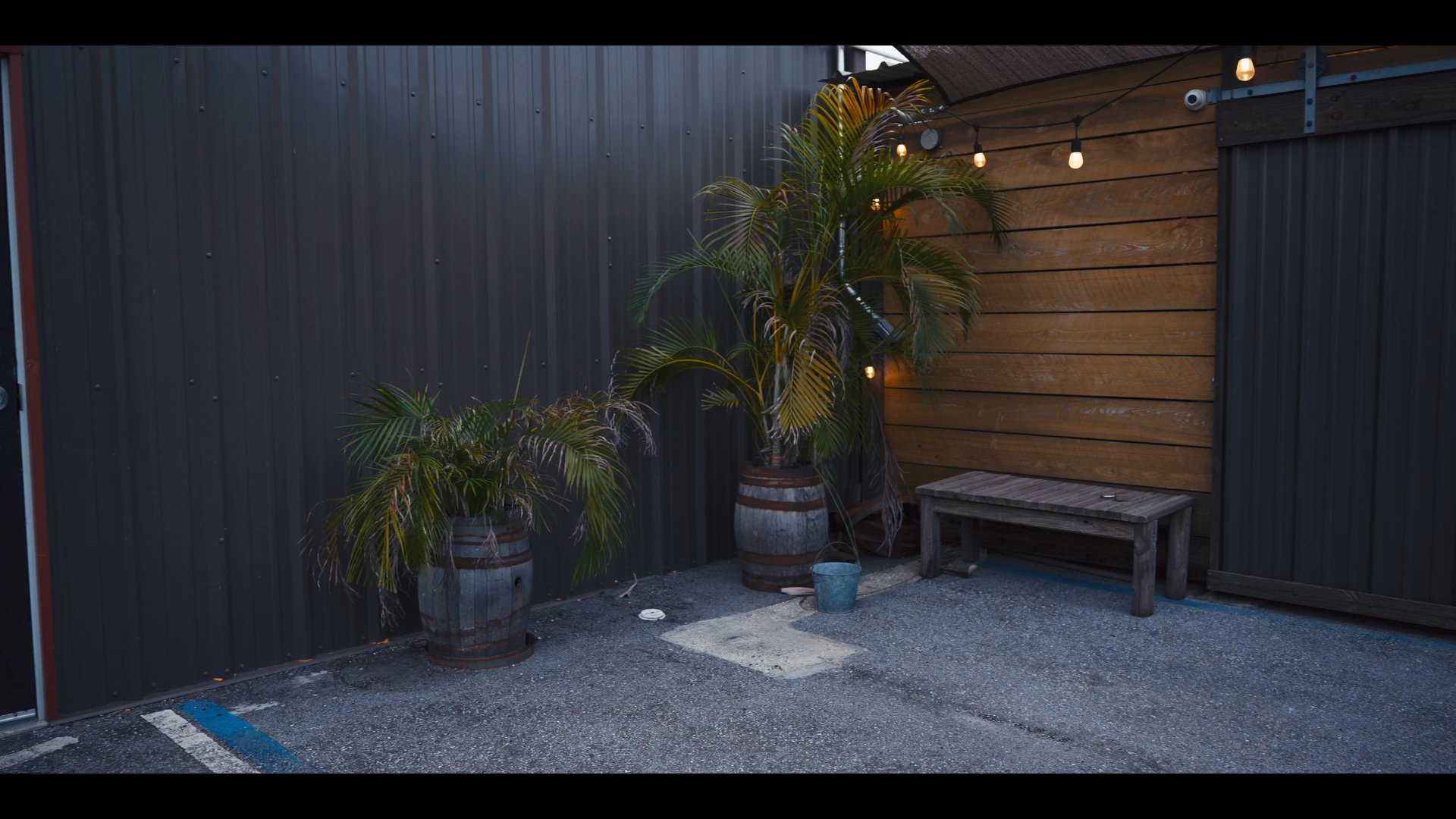 A man walks across a dimly lit outdoor courtyard to open a door and enter an indoor space, where he engages in a discussion with another individual.