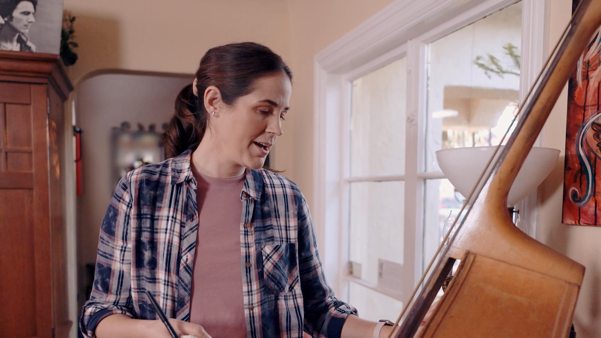 A man and a woman engage in a thoughtful conversation while standing near a double bass in a residential living space. They exchange ideas and coordinate details in a collaborative environment.