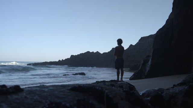 A young man observing waves from the sea crashing on rocks