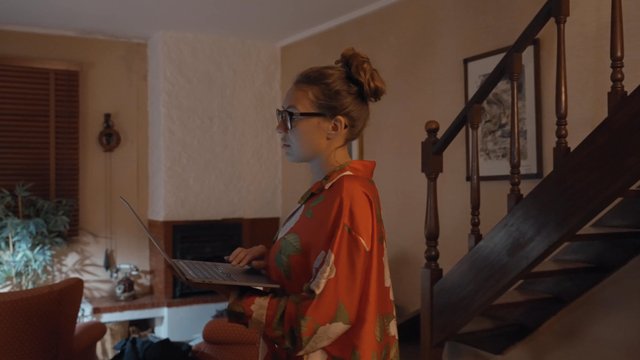 A girl walking around the room holding a laptop in her hands