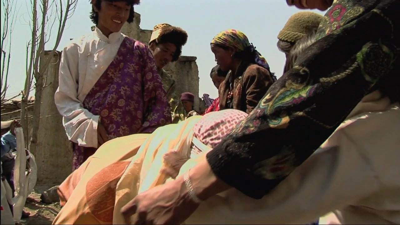 A visitor engages in a traditional welcoming ceremony with local residents in a remote Mustang village. The experience highlights meaningful community interaction against the backdrop of the region's distinctive landscape.