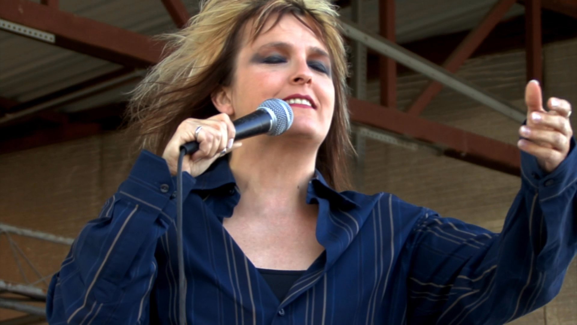 A female vocalist performs for an enthusiastic outdoor crowd during a live music concert. The singer interacts with the audience while delivering a high-energy vocal set.