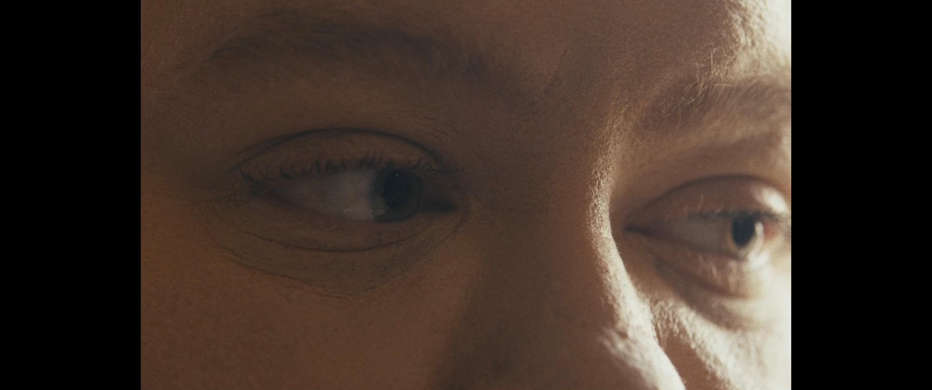 An individual sits in quiet reflection while listening to audio on a smartphone. The camera captures close-up shots of the subject's face transitioning between pensive and relaxed expressions.