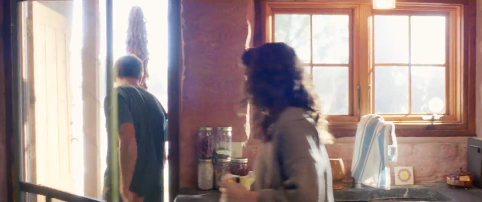 A man and woman experience a tense interaction within a rustic kitchen setting, resulting in the man silently exiting the home.