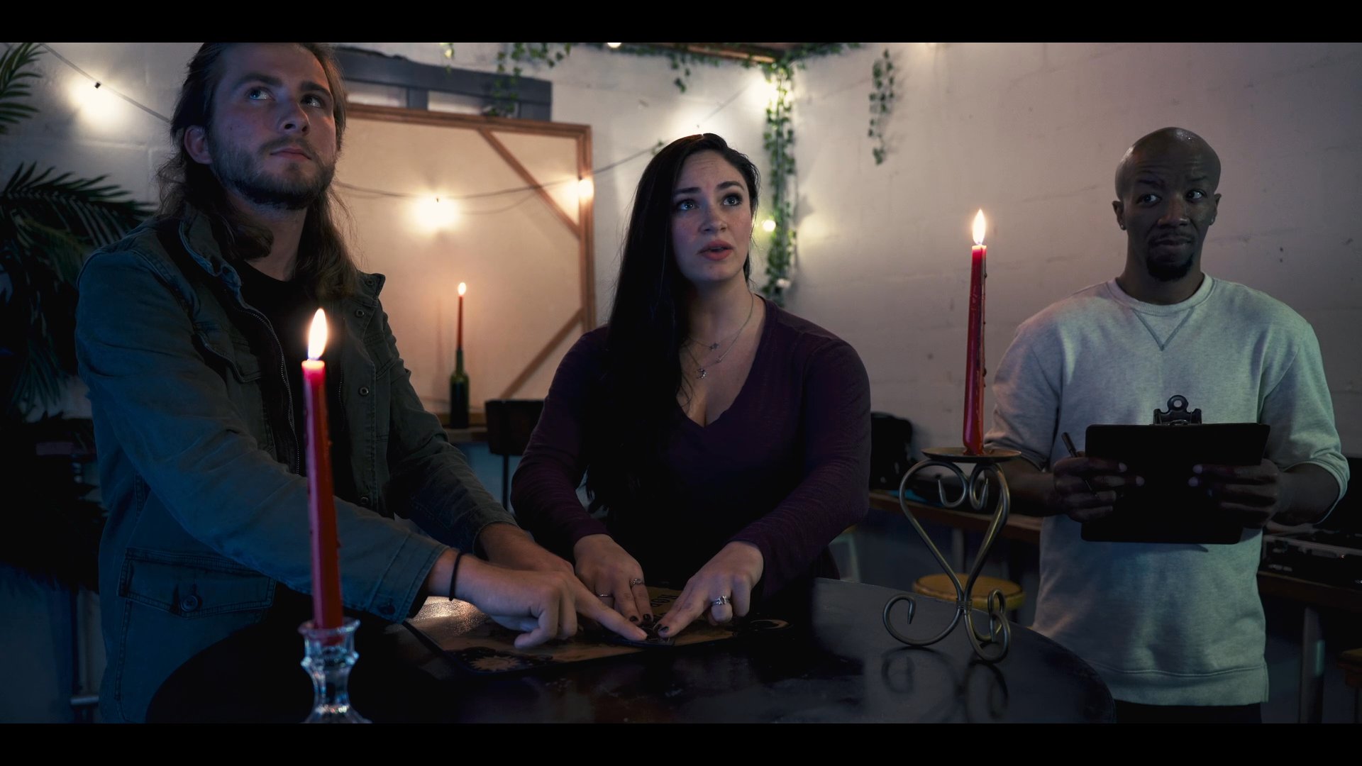 Three individuals conduct a séance around a ouija board by candlelight, attempting to communicate with the spirit realm.