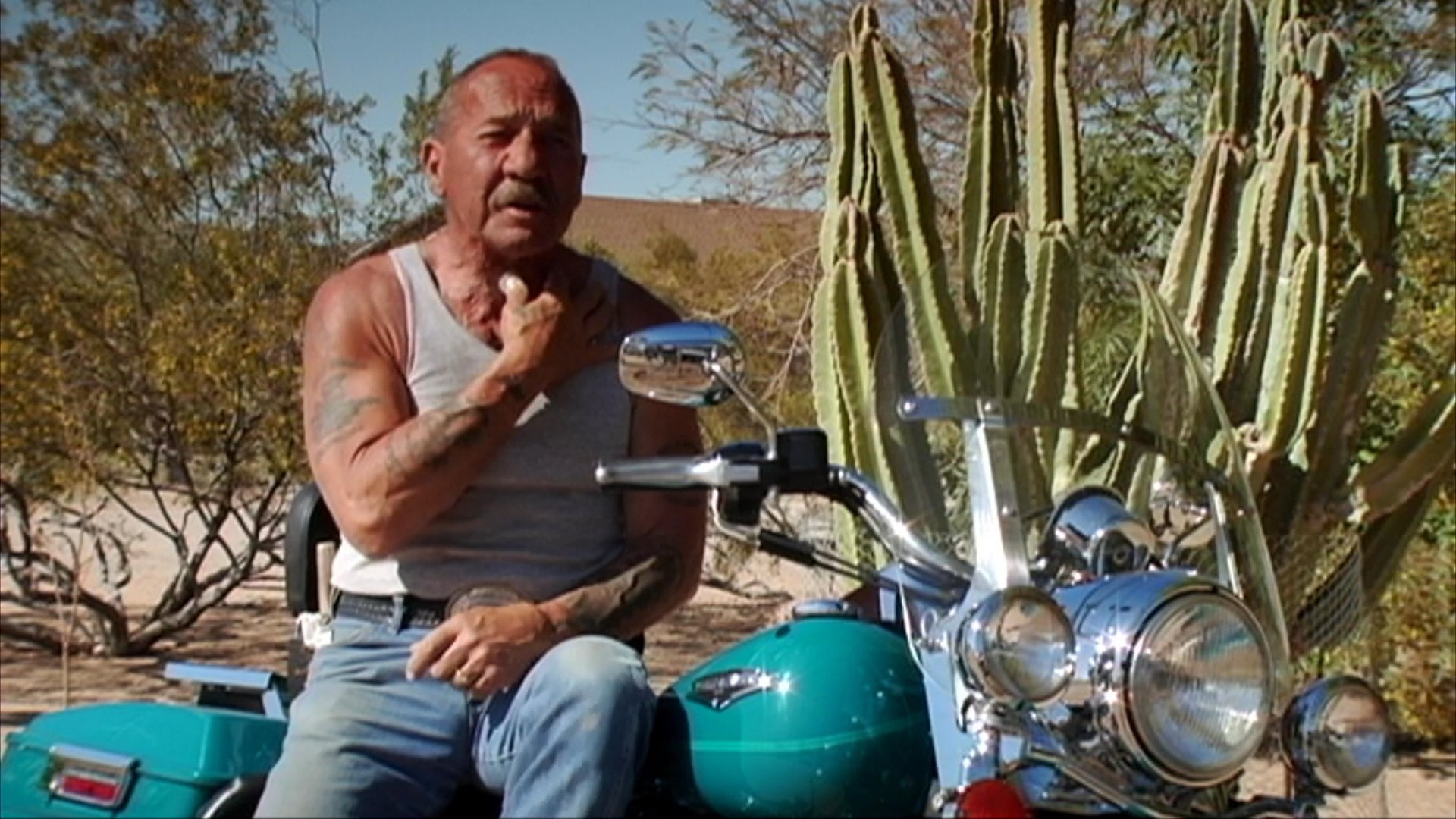 A live band performs a concert on stage, transitioning to an intimate interview with a man sitting on a motorcycle in a desert landscape.