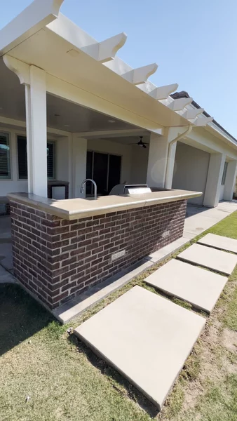 Brick outdoor bar with concrete countertop and white pergola, featuring concrete stepping stones