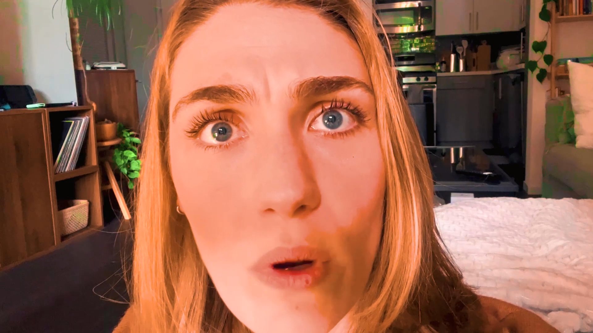 A woman addresses the camera directly, displaying a range of emotive facial expressions while speaking in a domestic setting.