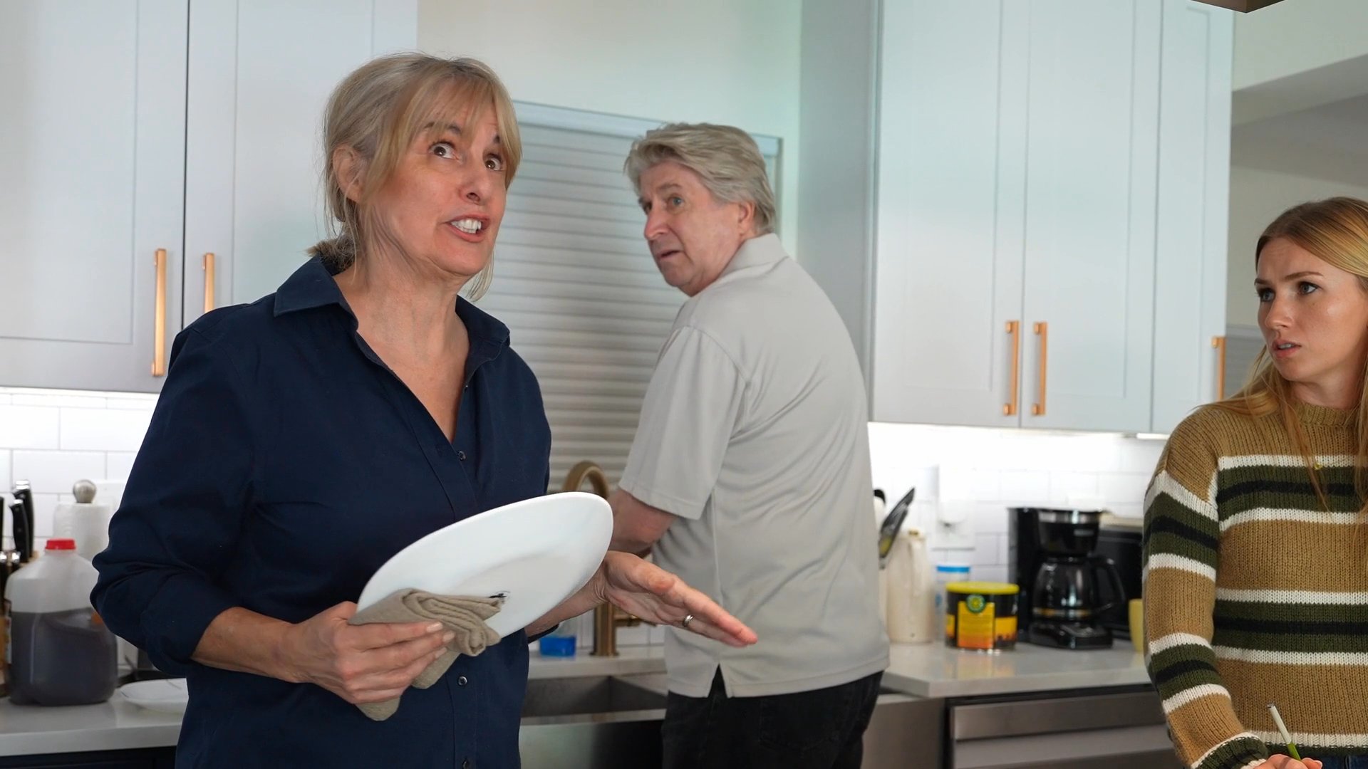Family members prepare a meal in the kitchen before welcoming guests arriving with beverages for the holiday celebration.