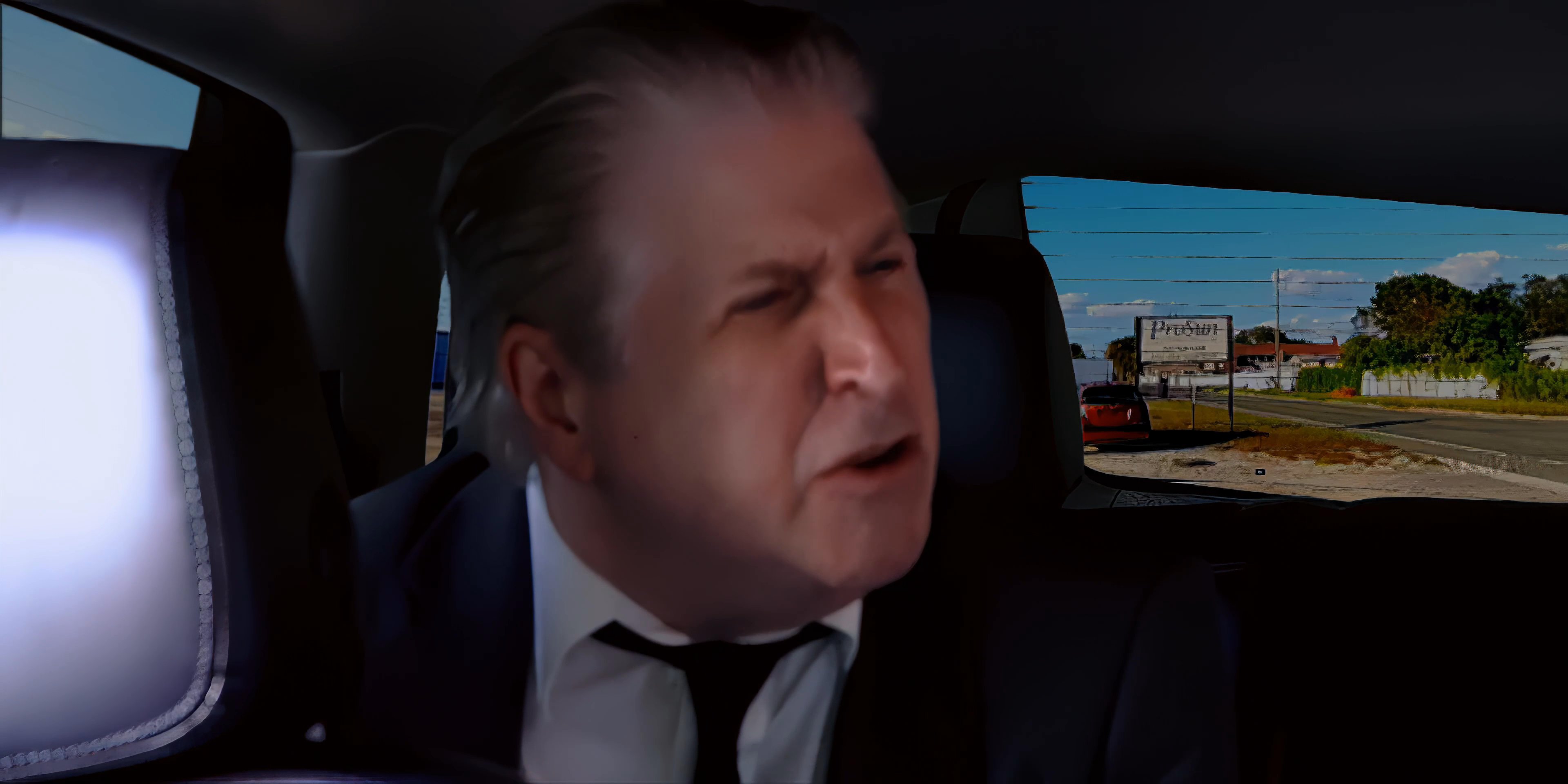 Two men engage in an intense verbal exchange while sitting in the back of a moving vehicle.