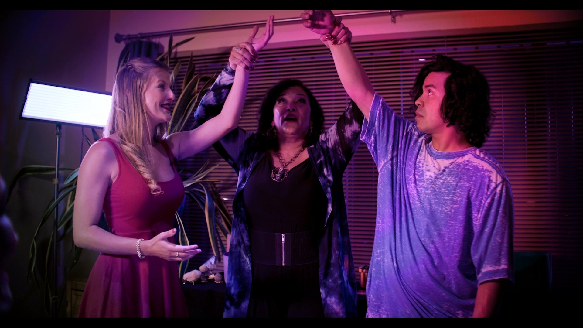 A group of three performers engage in a stylized, dramatic sequence featuring expressive gestures and glowing mystical light effects in a studio setting.