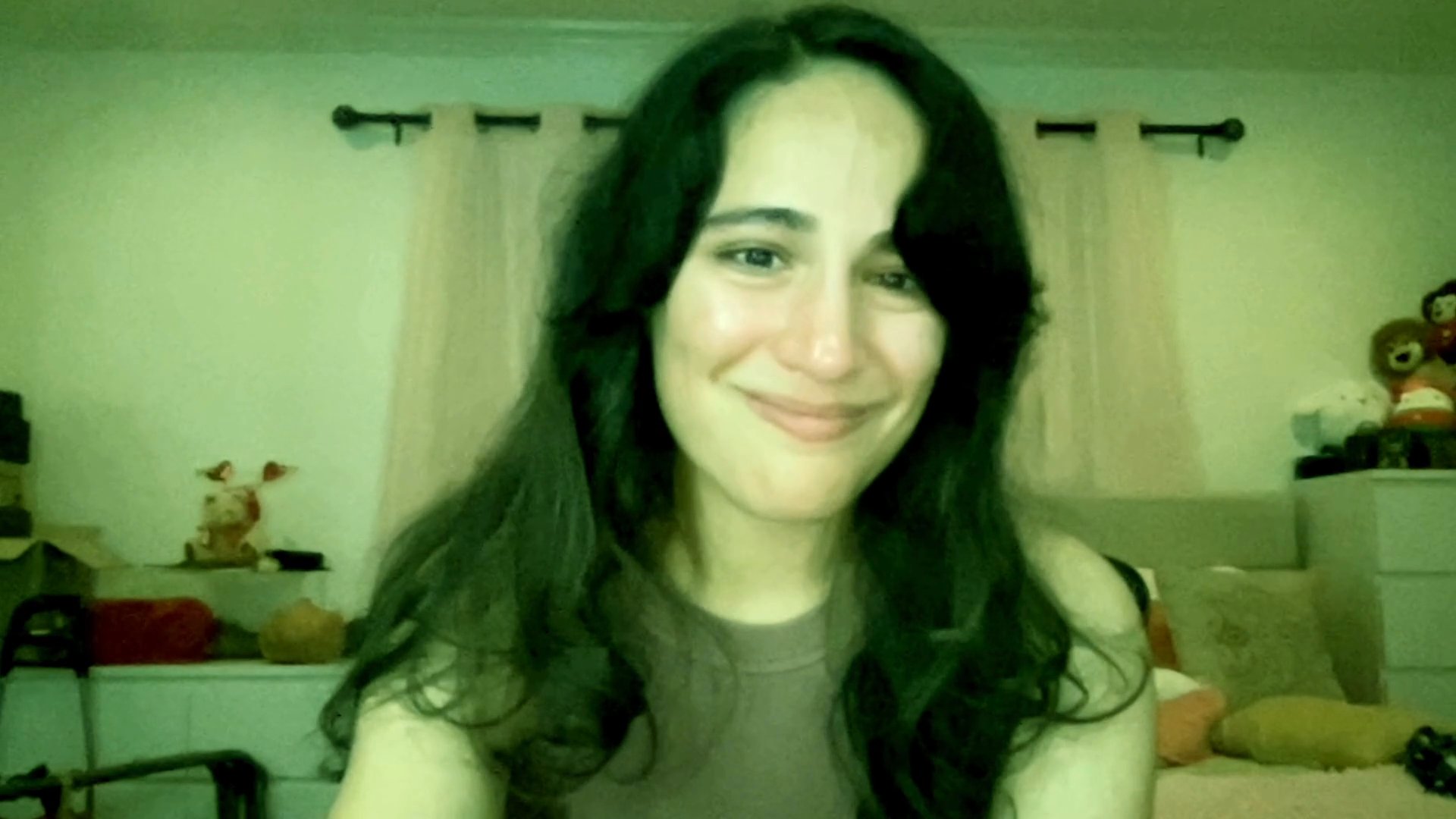 A woman shares an emotional experience while speaking directly to the camera in her bedroom. She exhibits a range of vulnerable expressions while discussing a personal narrative.