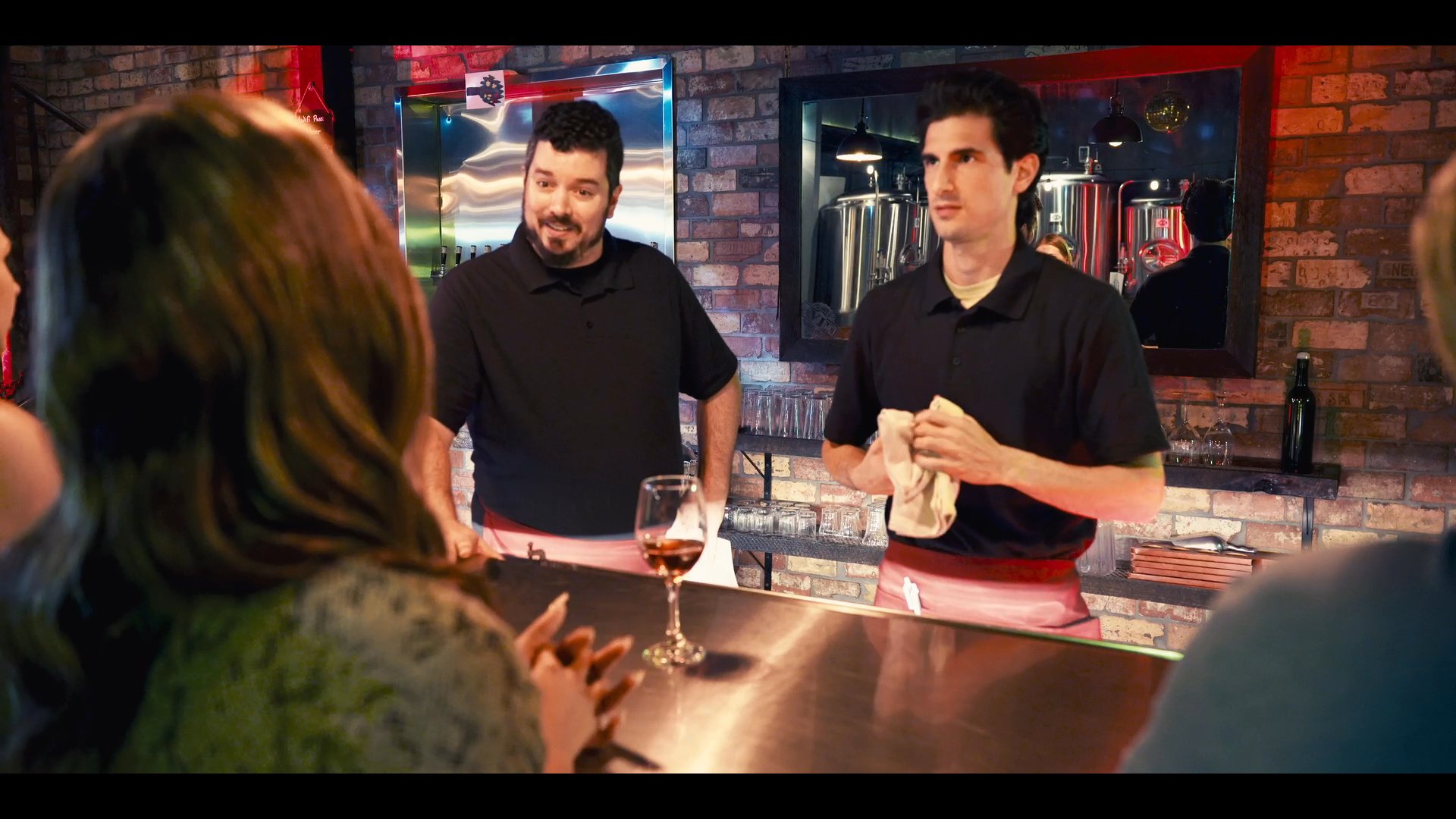 A patron engages in a professional discussion with restaurant staff at a bar counter while employees demonstrate service procedures. The interaction occurs within a contemporary dining venue, highlighting customer service dynamics.