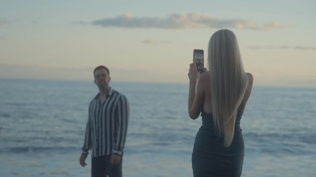 A woman photographs her boyfriend on the beach