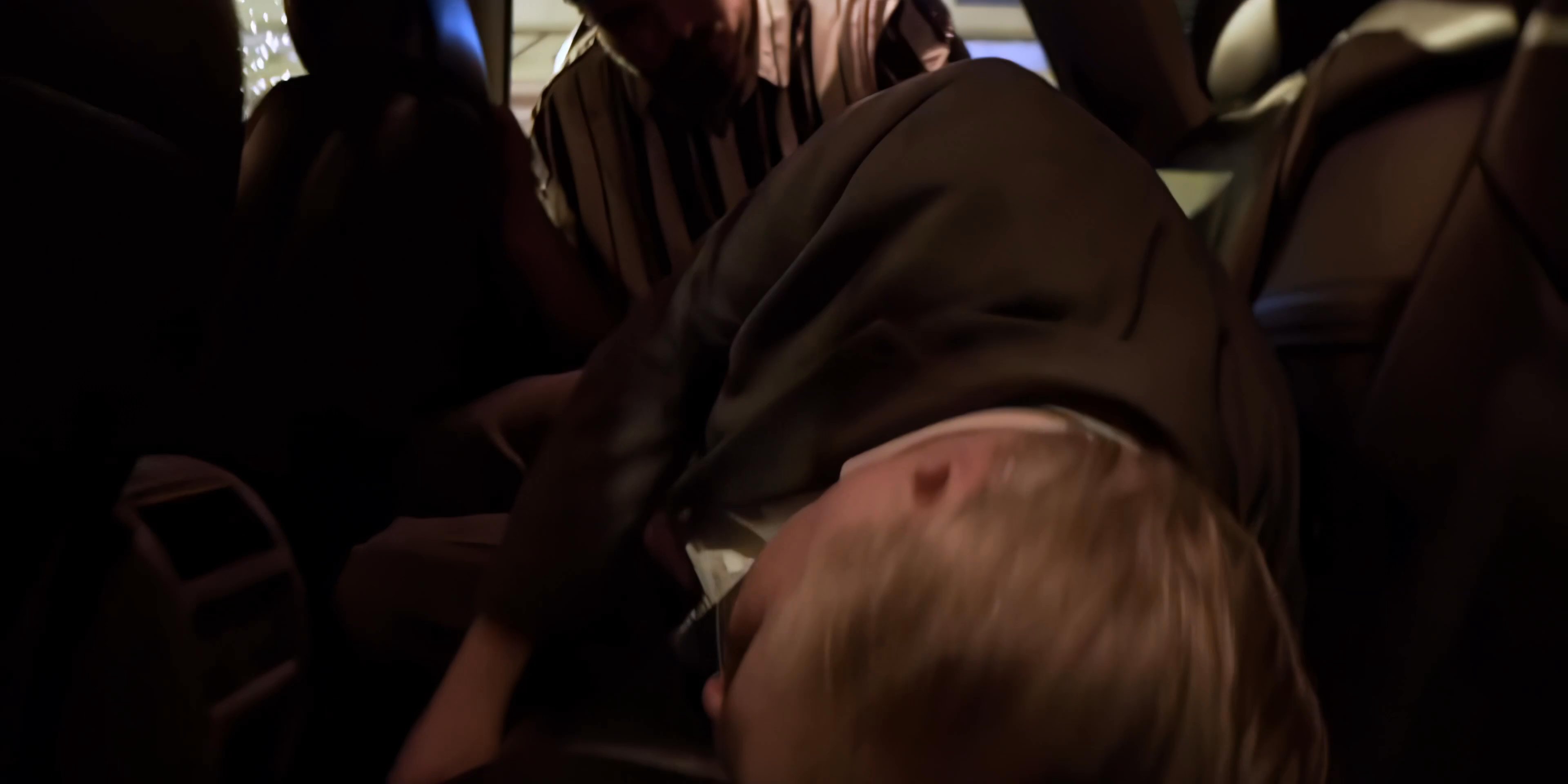 A man in a striped shirt engages in a physical struggle with another individual inside a parked vehicle at night. The situation escalates into a forceful physical confrontation.