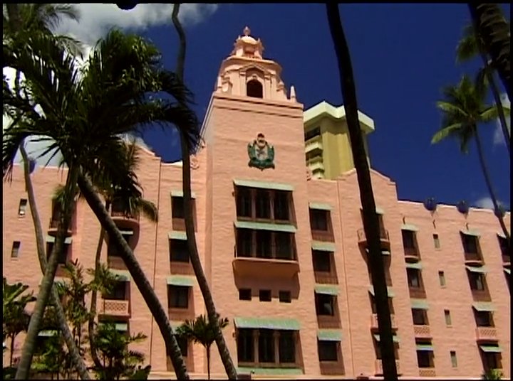 Historical archival footage of legendary surfer Duke Kahanamoku transitions to modern scenes of the Royal Hawaiian Hotel and contemporary surfers in Waikiki. This visual narrative captures the enduring cultural significance of surfing in Hawaii.