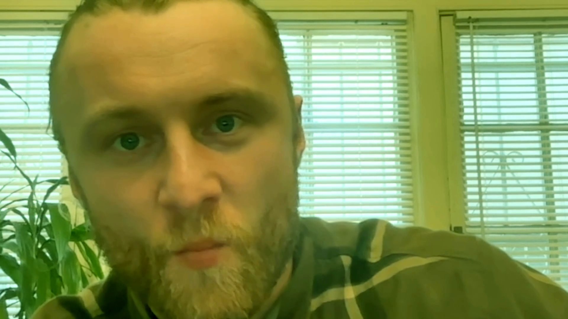 A man addresses the camera, engaging in a direct and focused conversation while sitting in an indoor setting.