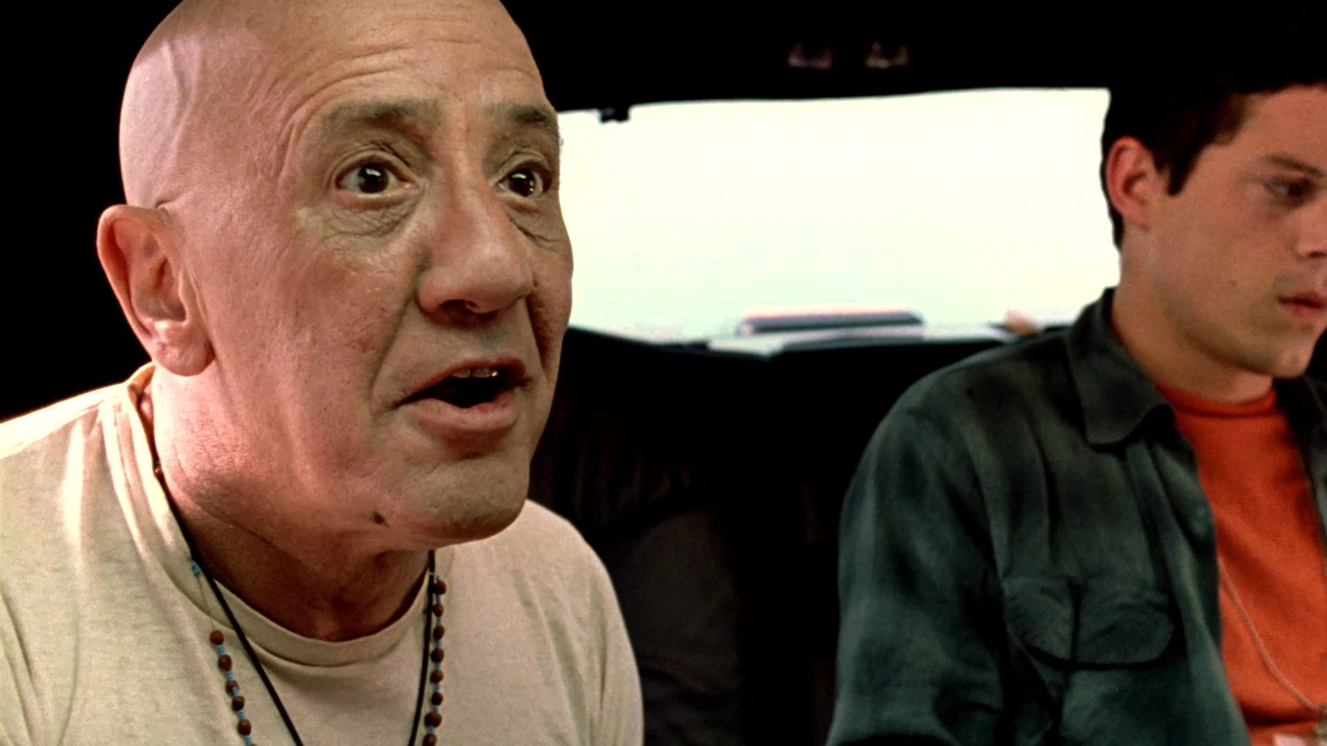 Three individuals engage in an intense, serious conversation while traveling as passengers in the back of a moving vehicle.