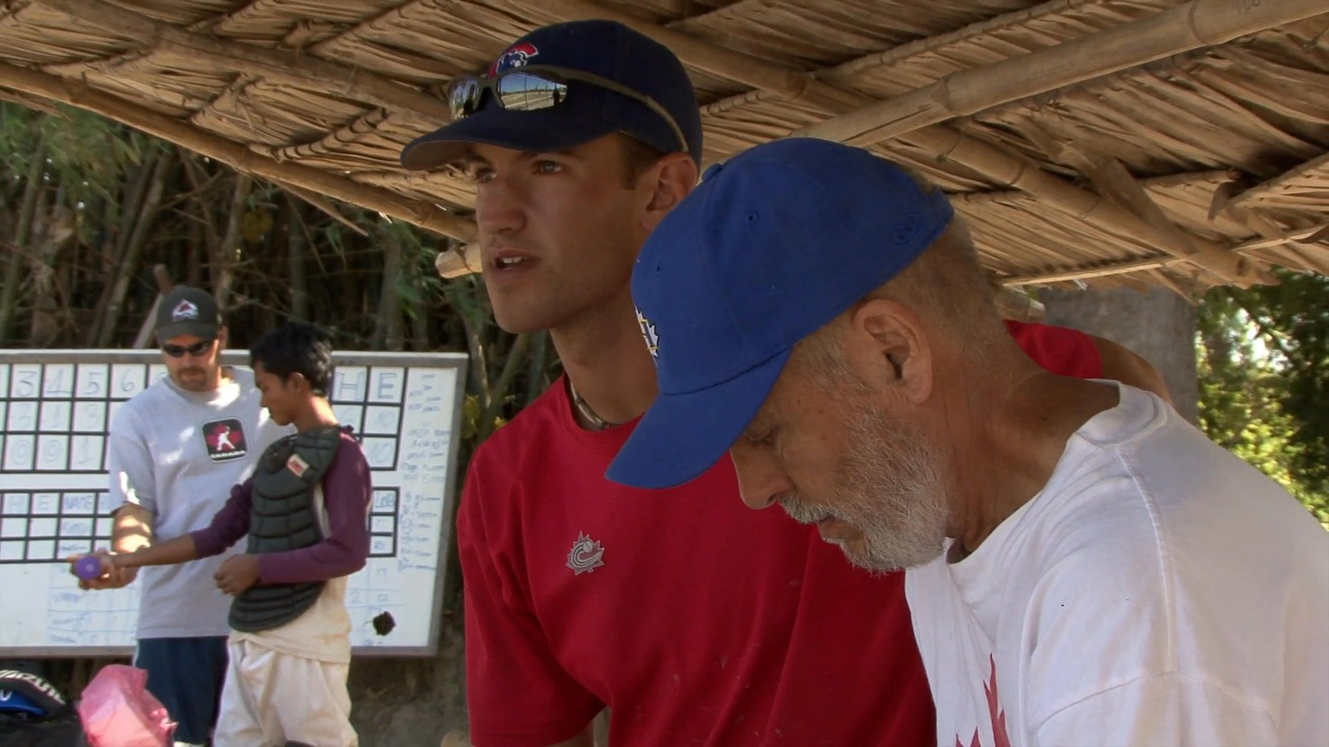 A baseball player discusses the program in Cambodia, followed by coaches reviewing equipment and providing instructional guidance to team members on an outdoor field.