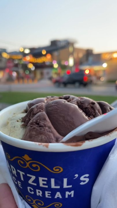 Hartzell's - Blue cup with 2 scoops of icecream: 1 chocolate, 1 dusty bean. A street in background with car, building, and flashing lights. - Ice Cream & Frozen Yogurt Near Me - Bloomington, Indiana