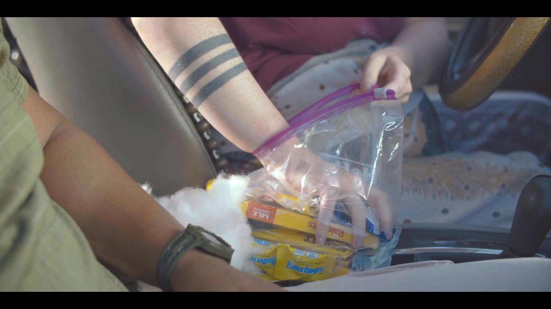 Two individuals engage in a lighthearted conversation while sharing snacks inside a passenger vehicle. The pair exhibits positive rapport through laughter and relaxed interaction during their journey.