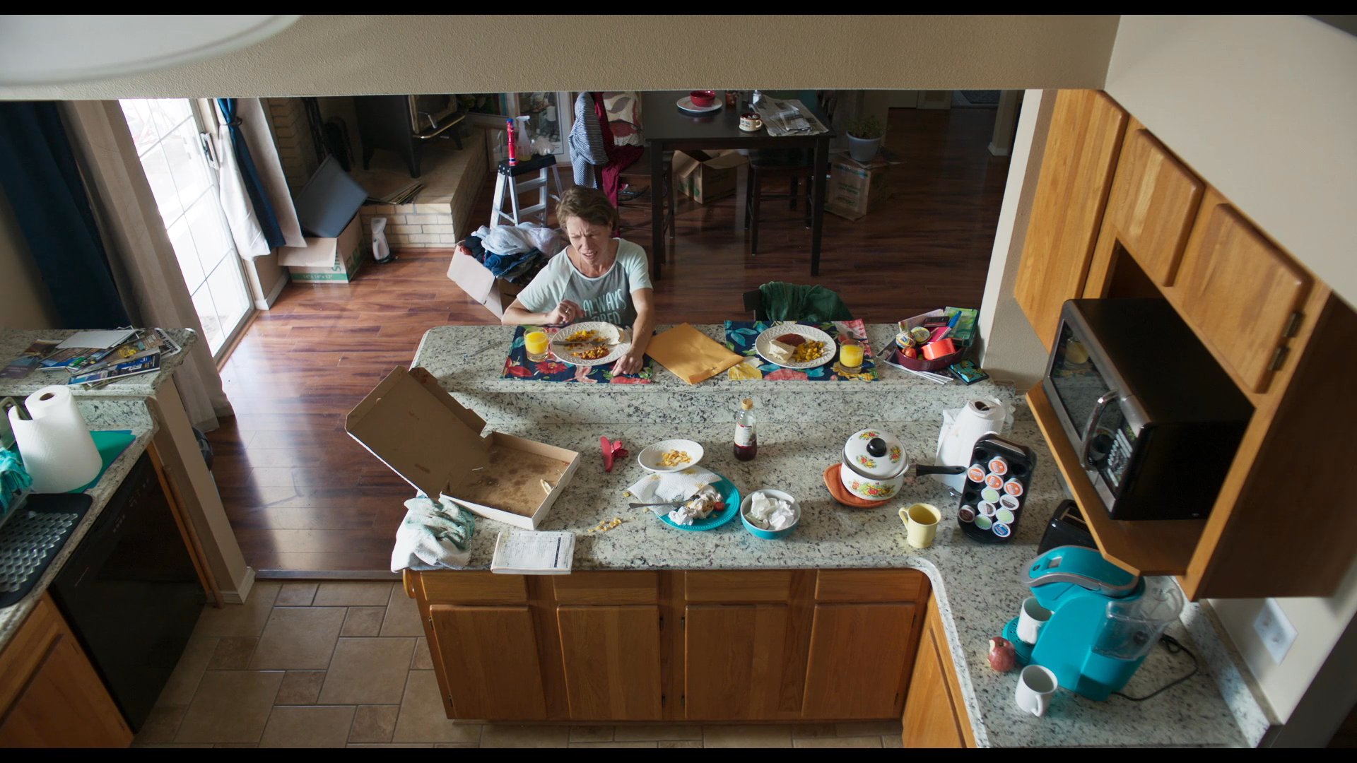 A woman finishes preparing a meal in a kitchen and appears visibly exhausted as she walks away from the counter. The scene captures the transition from domestic tasks to a state of fatigue.