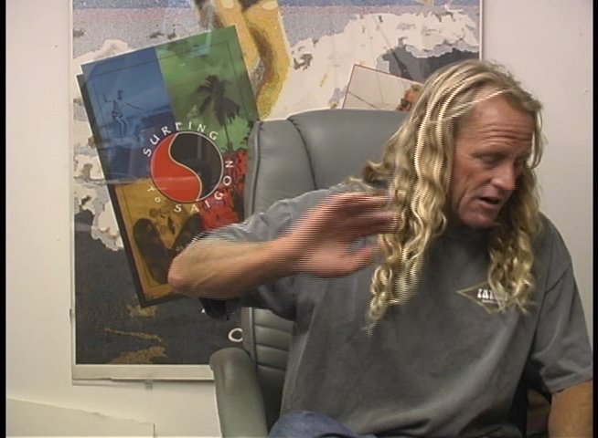 A long-haired male athlete sits in an office chair and engages in an interview, using hand gestures to emphasize his commentary.