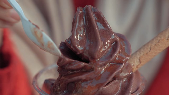 A girl tasting chocolate ice cream with a plastic spoon