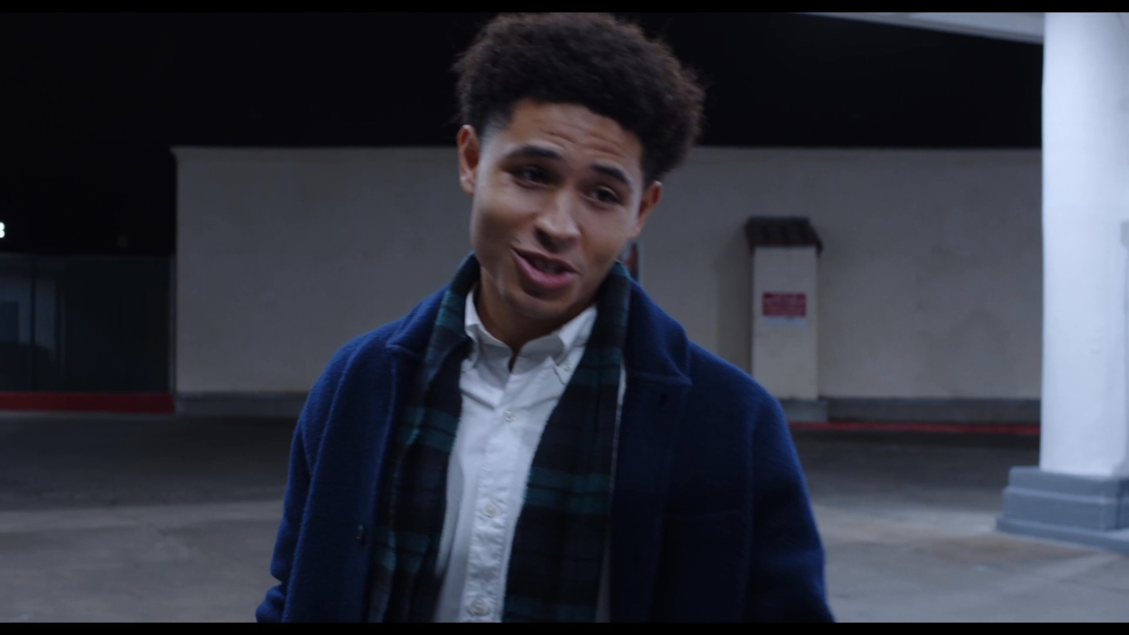 Two young men engage in a calm, night-time conversation while one sits in the open trunk of a vehicle parked at a gas station.