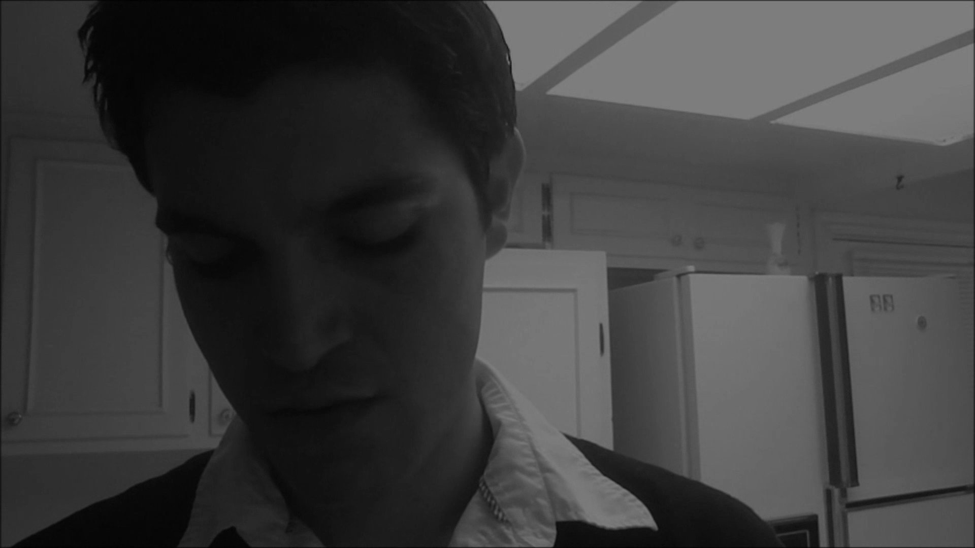 A man washes his hands in a kitchen sink before observing a handwritten note asking about a missing woman's whereabouts. The scene conveys a sense of quiet tension and personal concern.